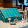 The Complete Cocktail Set displayed on a table, featuring a shaker, jigger, strainer, and glass in a stylish box.