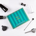 Colorful box of The Complete Cocktail Set surrounded by bar tools for mixing drinks at home.