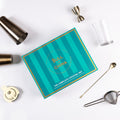 The Complete Cocktail Set displayed with tools like a shaker, jigger, and strainer on a striped background.